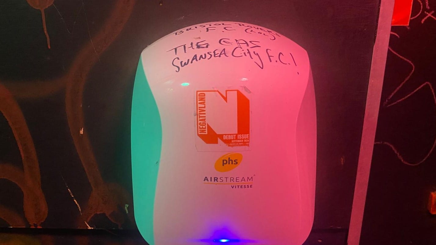 A hand drier in a pub toilet with Negativland's orange and white logo sticker on it