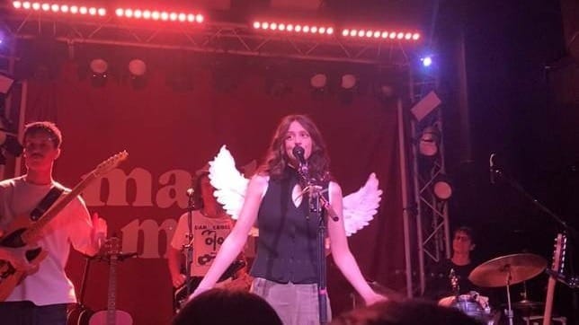 A person singing on a stage with wings and a band on it

AI-generated content may be incorrect.